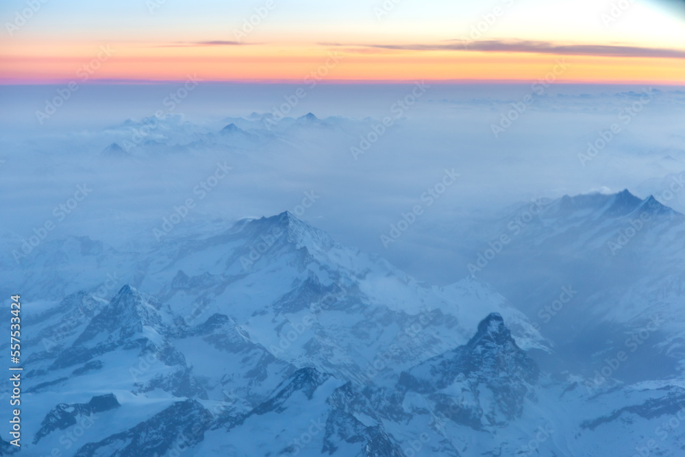 The Alps at sunrise with light fog and orange sky.