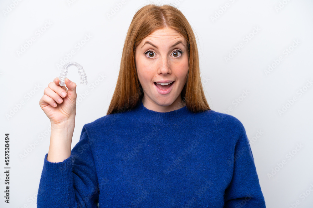 Young redhead woman holding invisible braces isolated on white background with surprise and shocked facial expression Young redhead woman holding invisible braces isolated on white background with surprise and shocked facial expression