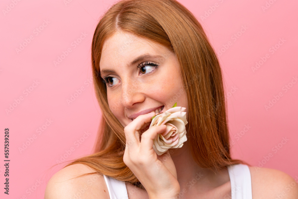 Young redhead woman isolated on pink background holding flowers. Close up portrait Young redhead woman isolated on pink background holding flowers. Close up portrait