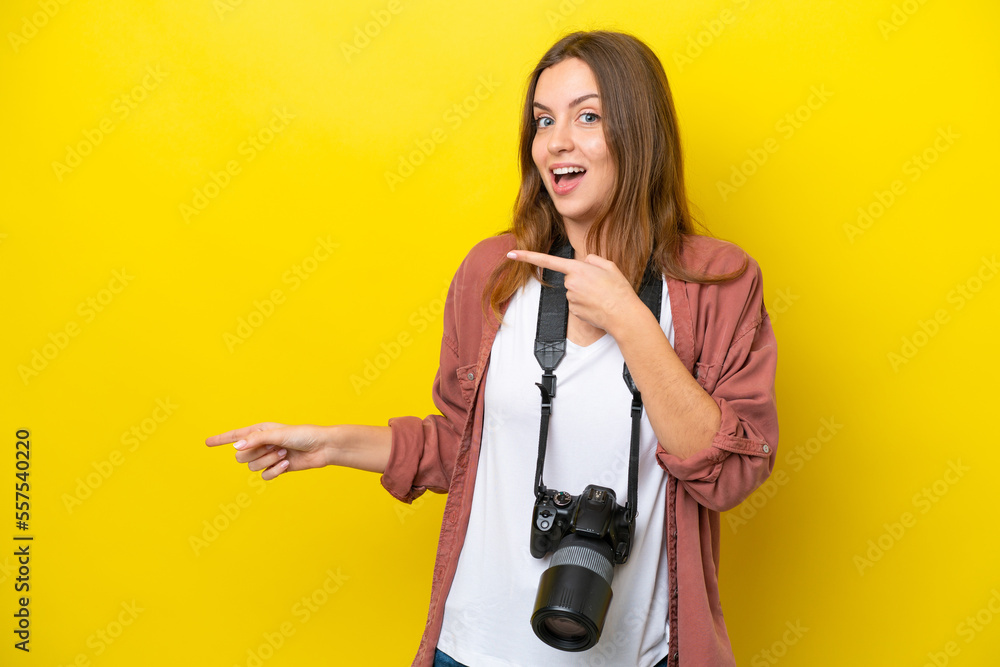 Young photographer caucasian woman isolated on yellow background surprised and pointing side Young photographer caucasian woman isolated on yellow background surprised and pointing side