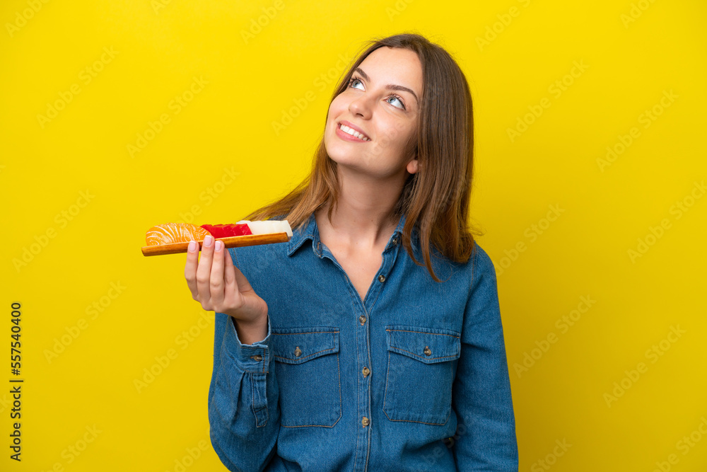 Young caucasian woman holding sashimi isolated on yellow background looking up while smiling Young caucasian woman holding sashimi isolated on yellow background looking up while smiling