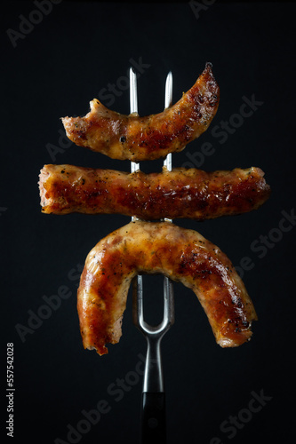 Grilled sausages with veal on a fork. Delicious lunch concept for hotel or restaurant on black background.