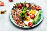 Plate with fried eggs, bacon, avocado, strawberries and fresh salad on a light background. Ketogenic diet food, healthy meal concept, Long banner format. top view