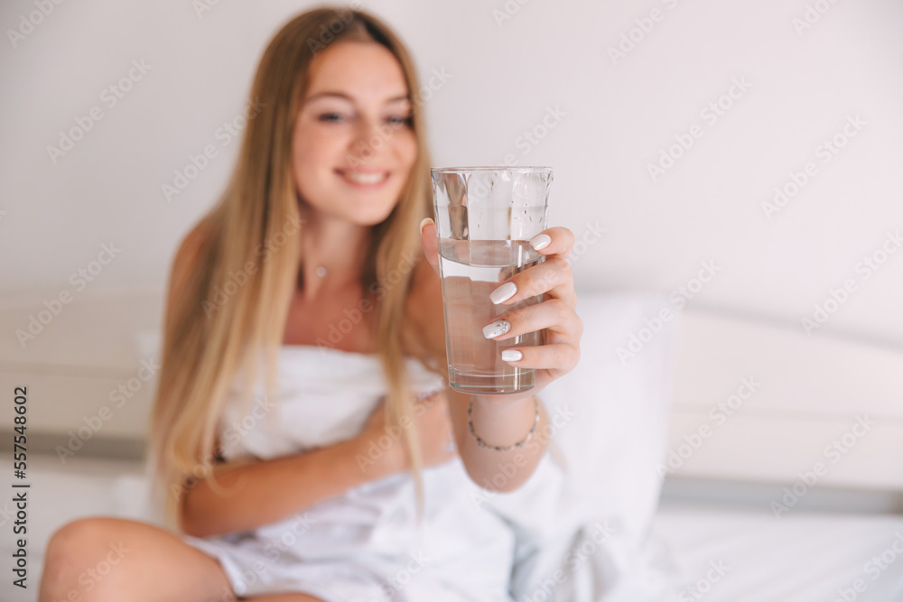Happy beautiful woman drink water during wake up on morning at the bedroom. Smiling girl holding transparent glass on bed. Happy beautiful woman drink water during wake up on morning at the bedroom. Smiling girl holding transparent glass on bed.