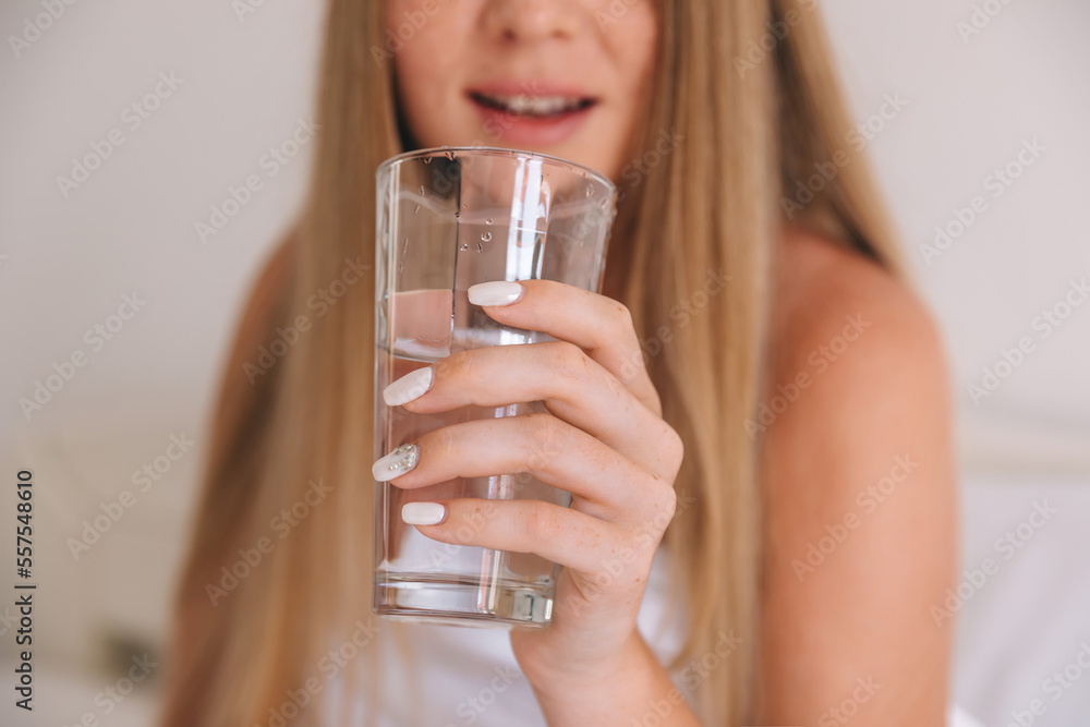 Young woman holding water glass, female drinking pure water on bed at home. Healthy, Refreshment, lifestyle concept Young woman holding water glass, female drinking pure water on bed at home. Healthy, Refreshment, lifestyle concept