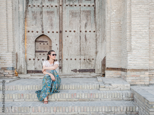 Beautiful young woman against the backdrop of landmarks and ancient buildings. Sights of ancient cities of Uzbekistan. Clear, sunny day. Vacation and travel concept #557558826