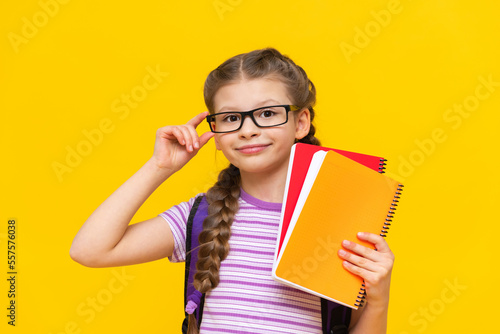 A cute schoolgirl in a striped T-shirt holds notebooks in her hand.