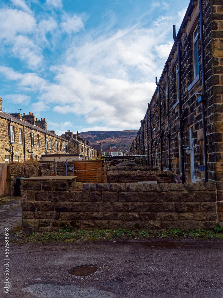 Back gardens of stone built terraced houses in likely Town in west Yorkshire with Ilkley Moor in the Background under a blue sky.