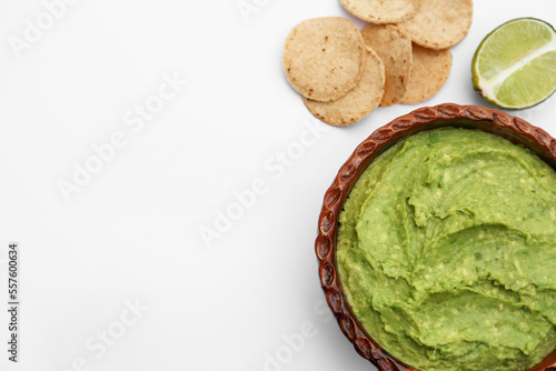 Delicious guacamole made of avocados, lime and chips on white background, flat lay. Space for text