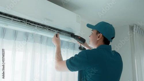 An Asian young Technician service man wearing blue uniform checking ,  cleaning air conditioner in home
