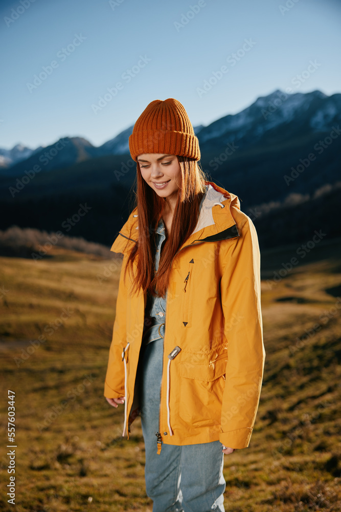 Woman running up the hill to the camera smile with teeth in the mountains in the autumn in a yellow raincoat and jeans happy sunset trip on a hike mountains in the snow, freedom lifestyle 
