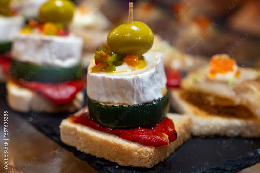 Fototapeta premium Typical snack of Basque Country, pinchos or pinxtos skewers with small pieces of bread, sea food, eggs, cheese, jamon served in bar in San-Sebastian or Bilbao, Spain