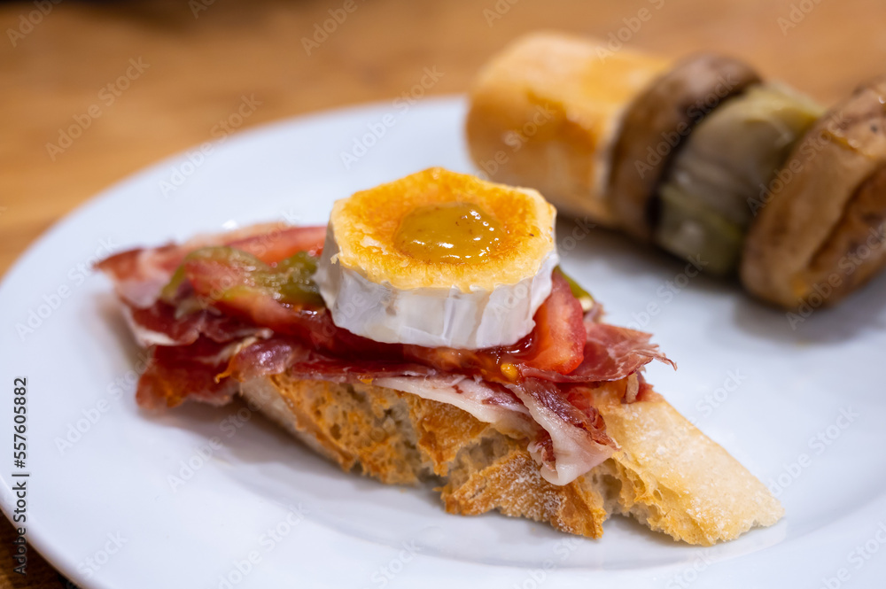 Fototapeta premium Board with typical snacks of Basque Country, pinchos or pinxtos, skewers or small piece of bread with toppings, served in bar in San-Sebastian or Bilbao, Spain