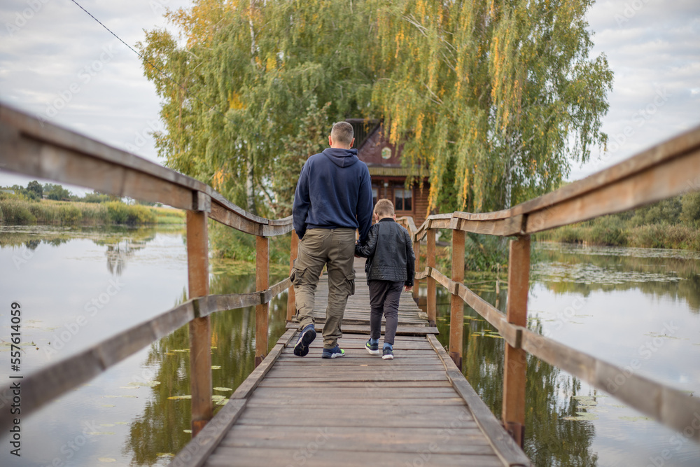 Happy father and son hugging and playing together in green nature. Fisherman's house with a wooden pedestrian bridge on a tiny island in the middle of the lake.