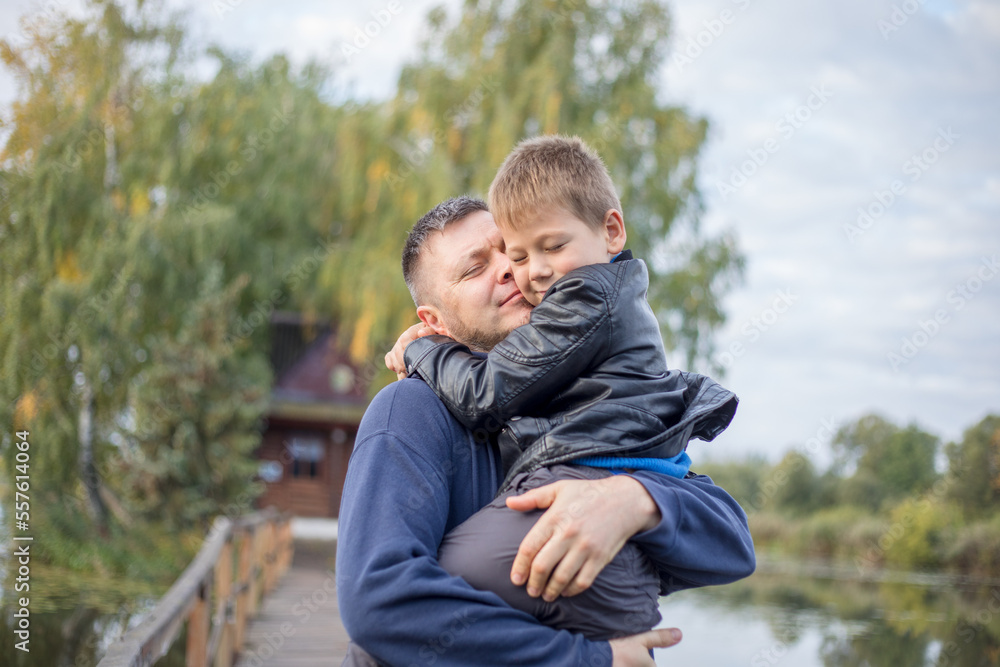 Happy father and son hugging and playing together in green nature. Fisherman's house with a wooden pedestrian bridge on a tiny island in the middle of the lake. Happy father and son hugging and playing together in green nature. Fisherman's house with a wooden pedestrian bridge on a tiny island in the middle of the lake.
