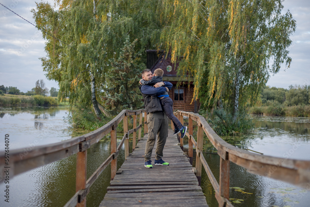 Happy father and son hugging and playing together in green nature. Fisherman's house with a wooden pedestrian bridge on a tiny island in the middle of the lake. Happy father and son hugging and playing together in green nature. Fisherman's house with a wooden pedestrian bridge on a tiny island in the middle of the lake.