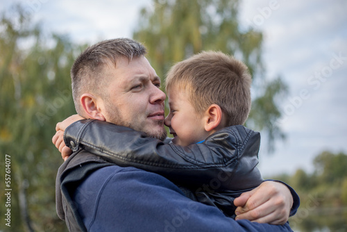 Happy father and son hugging and playing together in green nature. Fisherman's house with a wooden pedestrian bridge on a tiny island in the middle of the lake.