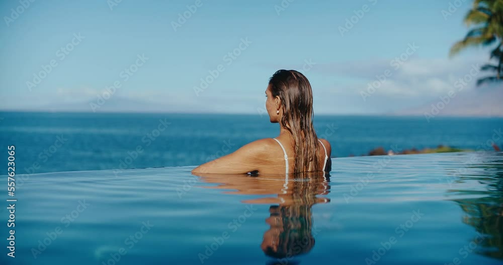 Woman relaxing in luxury infinity pool looking out at the ocean, tropical resort spa vacation Woman relaxing in luxury infinity pool looking out at the ocean, tropical resort spa vacation