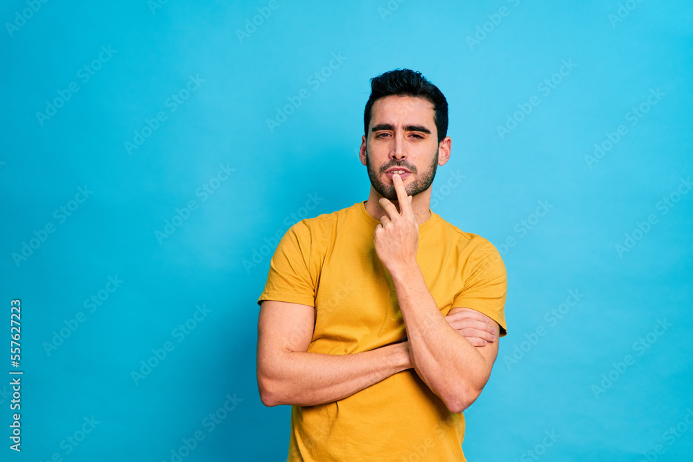 Young bearded male in yellow shirt touching chin and looking at camera while standing against blue background Young bearded male in yellow shirt touching chin and looking at camera while standing against blue background