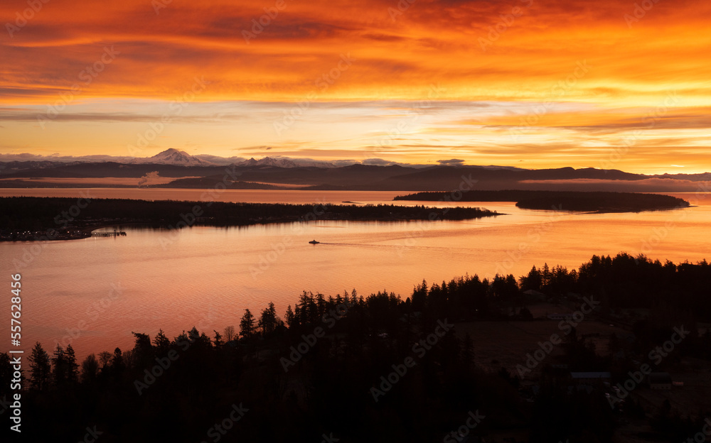 Sunrise Aerial View of Lummi Island and the Mainland With a Ferryboat Making a Morning Crossing. Just before the sun rises over the Cascade Mountains dramatic clouds form in the east and south. 