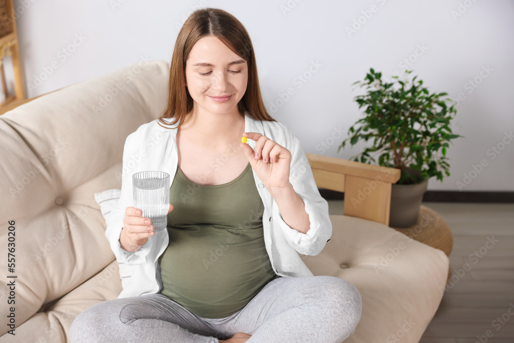 Beautiful pregnant woman holding pill and glass of water at home Beautiful pregnant woman holding pill and glass of water at home