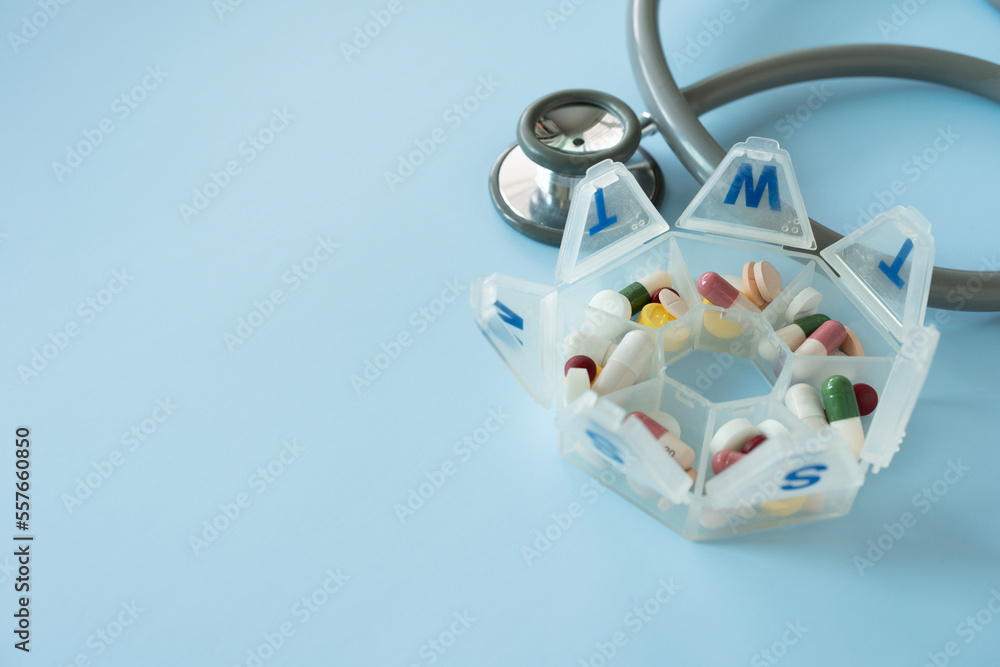 many colorful drug medicines or pill  in a pillbox with and  stethoscope on blue table, healthy and medicine concept