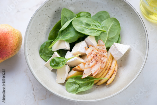 Salad with fresh spinach leaves, pear slices and camembert cheese served in a beige plate, middle close-up, horizontal shot