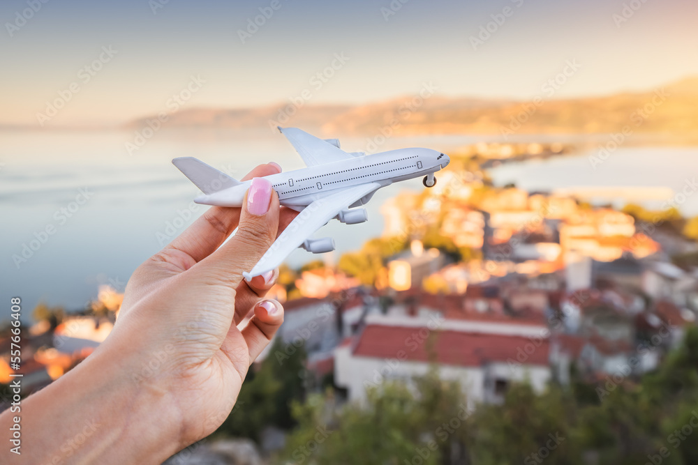 Naklejka premium Hand with toy airplane. Air transport ticket prices and travel concept. Resort sea town in the background
