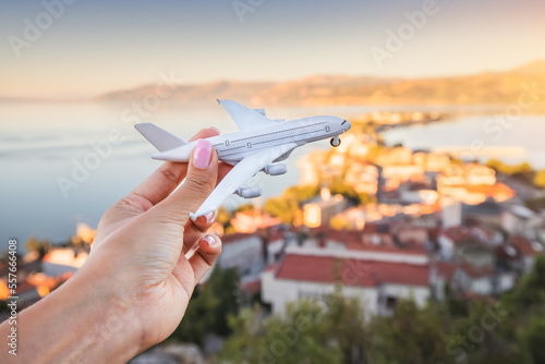 Hand with toy airplane. Air transport ticket prices and travel concept. Resort sea town in the background