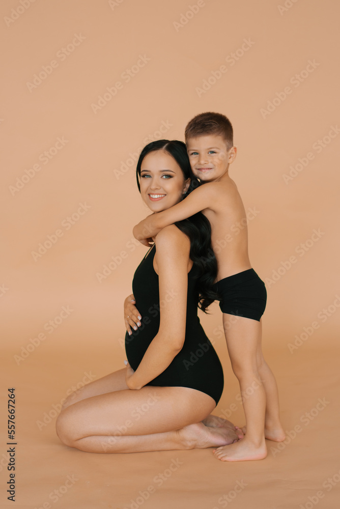 A happy young pregnant mother with her son on a beige background. The concept of a happy European or American family