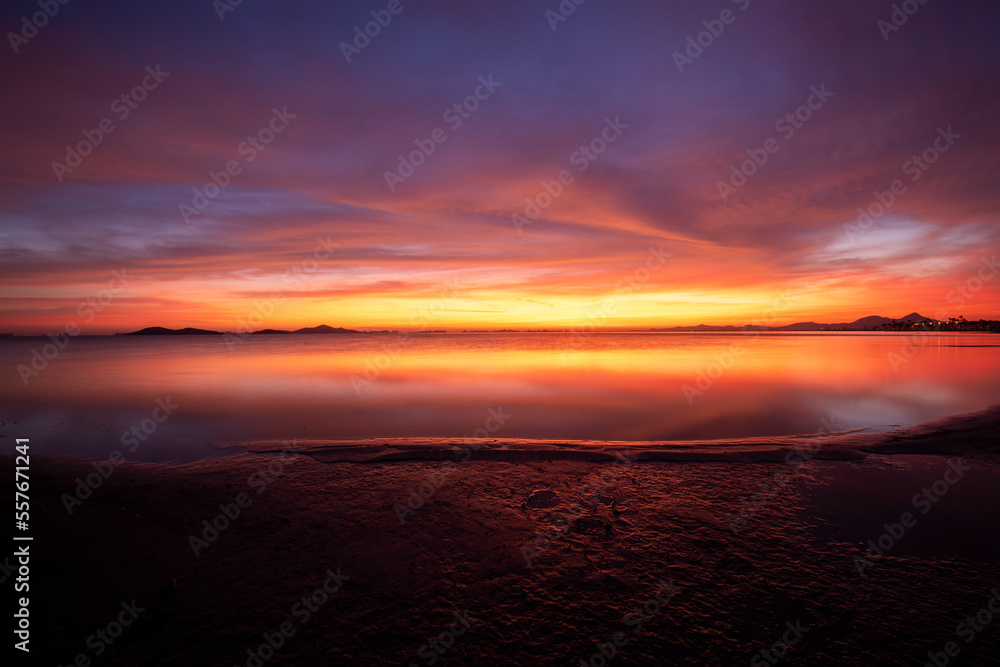 Idyllic orange sunrise on the beach of Los Urrutias, in the Mar Menor, Cartagena, Region of Murcia with the clouds reflecting in the calm waters of the sea