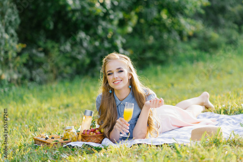 Pretty caucasian young woman with long hair is lying on a blanket in nature on a sunny summer day. Picnic, rest, relax in the fresh air.