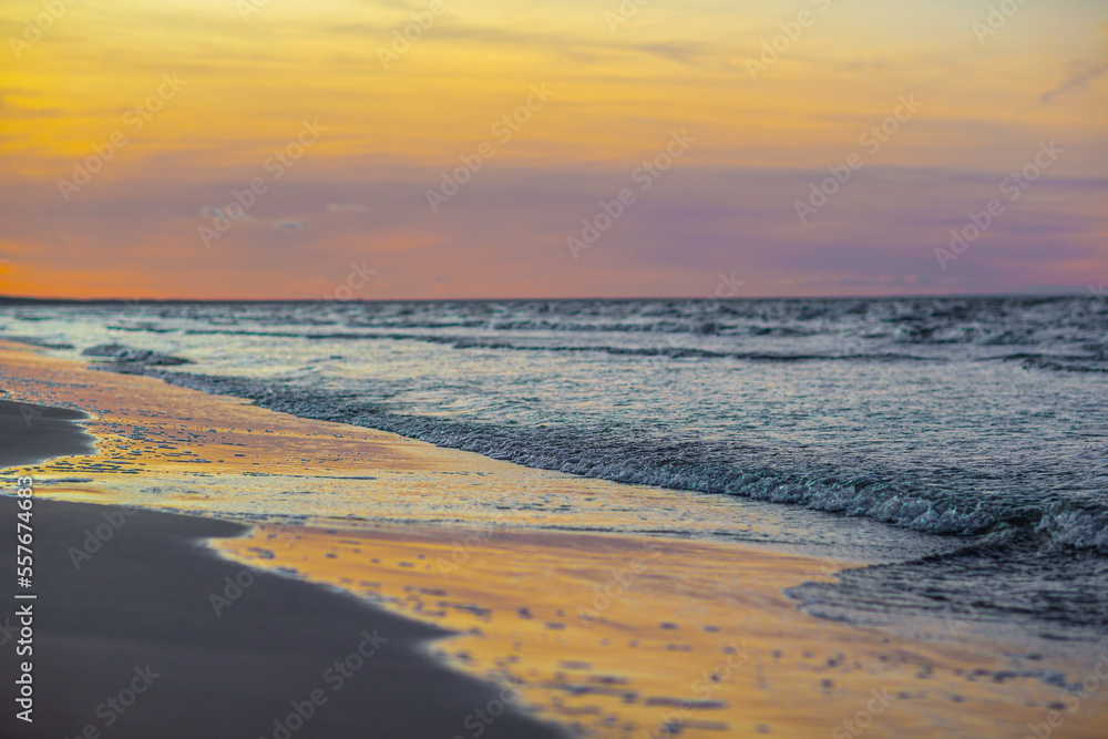 Photo of pink and yellow sunset over sea and small waves close up and reflection of the sky in the wet sand - Jurmala, Latvia