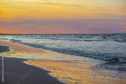 Photo of pink and yellow sunset over sea and small waves close up and reflection of the sky in the wet sand - Jurmala  Latvia