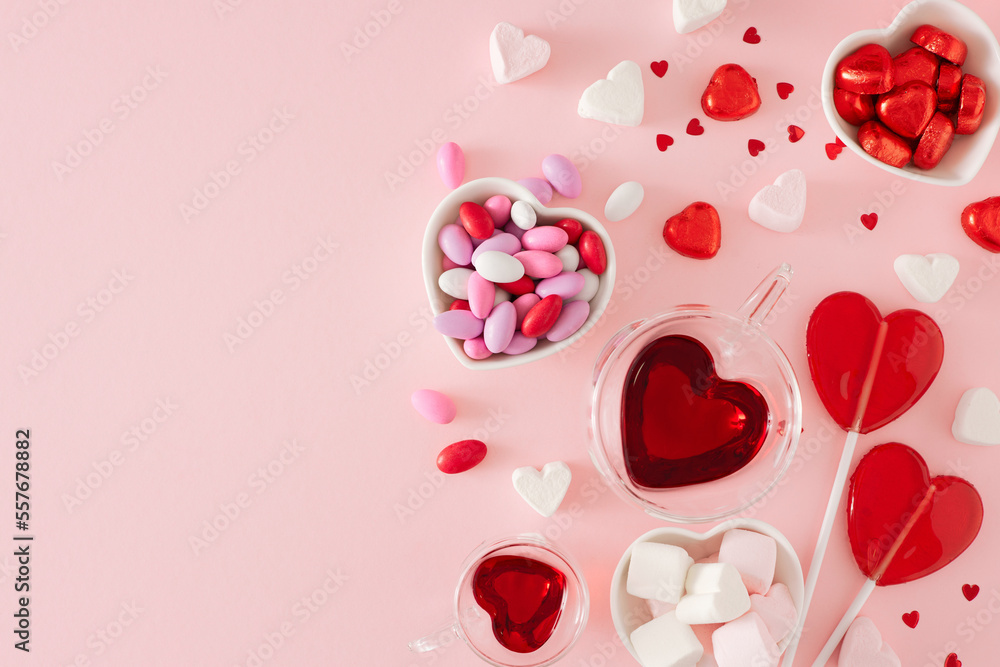 Valentines Day mood concept. Flat lay photo of heart shaped glass cup with drinking, chocolate candies and lollipops on pastel pink background with copy space. Sweet Valentines card idea. Valentines Day mood concept. Flat lay photo of heart shaped glass cup with drinking, chocolate candies and lollipops on pastel pink background with copy space. Sweet Valentines card idea.