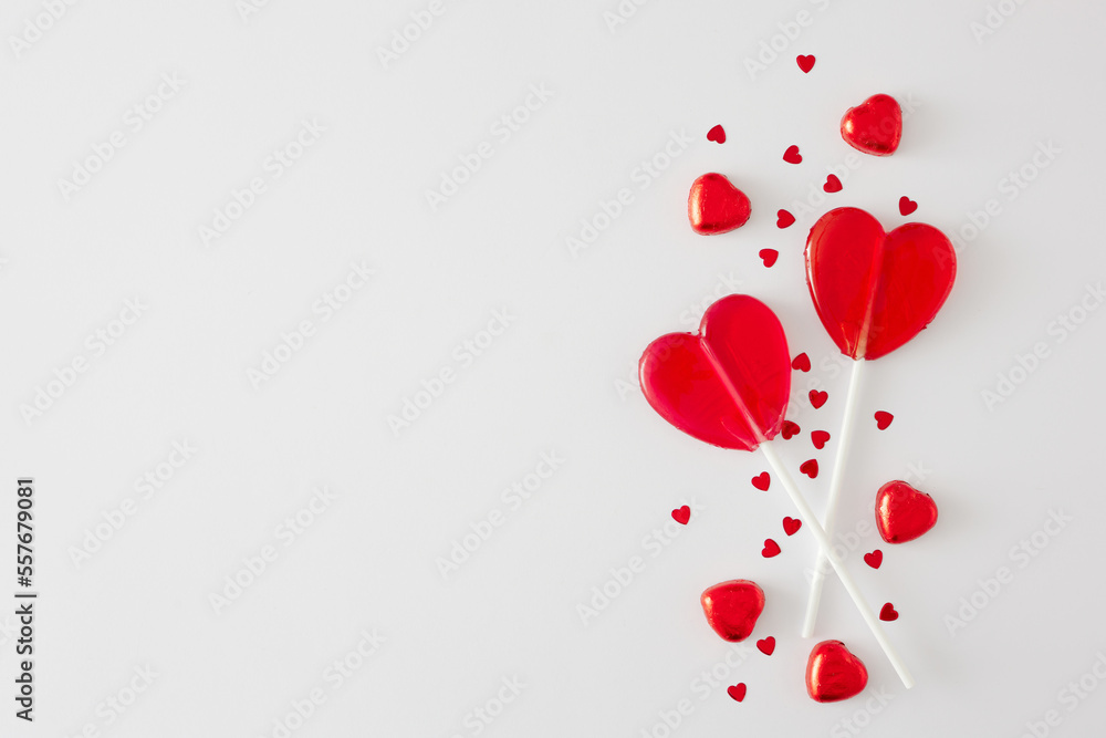 Sweet Valentines day concept. Flat lay composition of red heart shaped lollipops and hearts sprinkles on white background with copy space. Minimal Valentines card idea.
