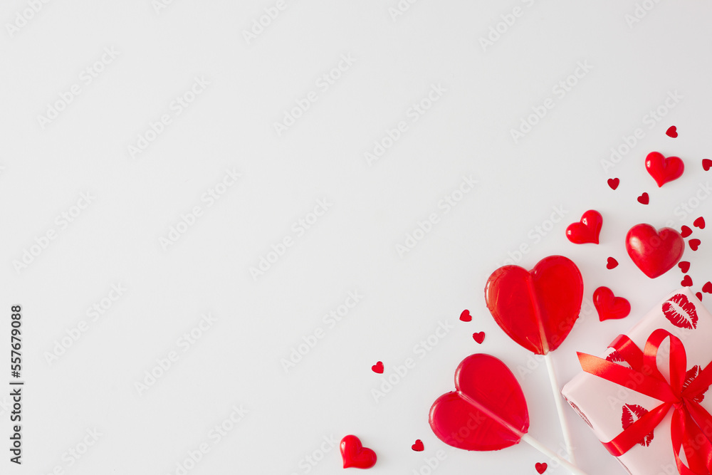 Mothers day or Valentines concept. Flat lay photo of gift boxes, red heart shaped lollipops and hearts sprinkles on white background with copy space. Minimal love card idea.