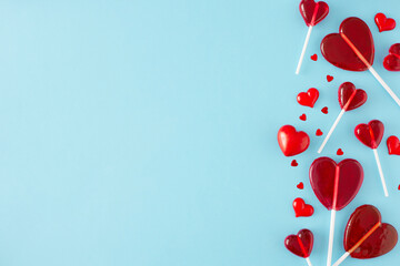 St Valentines Day concept. Flat lay photo of red heart shaped lollipops and sprinkles on pastel blue background with copy space. Sweet Valentines card idea.