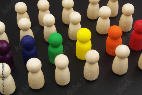 LGBT community concept. People figures colored in rainbow colors in crowd of uncolored wooden people figures on black background.