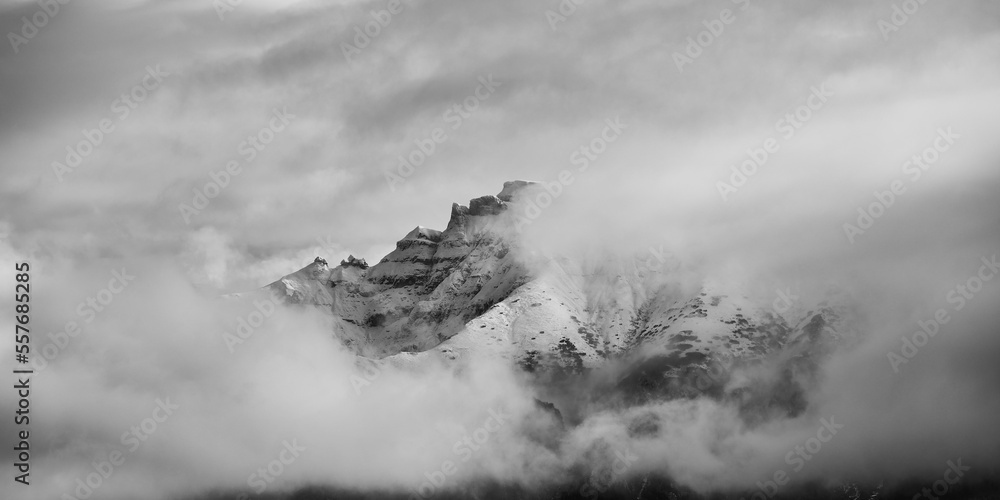 Black and white panoramic landscape of mountain top covered by snow and clouds