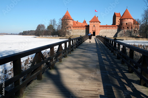 Château insulaire en brique rouge de Trakai en Lituanie, accessible par un pont en bois qui surplombe le lac gelé entourant le bâtiment.