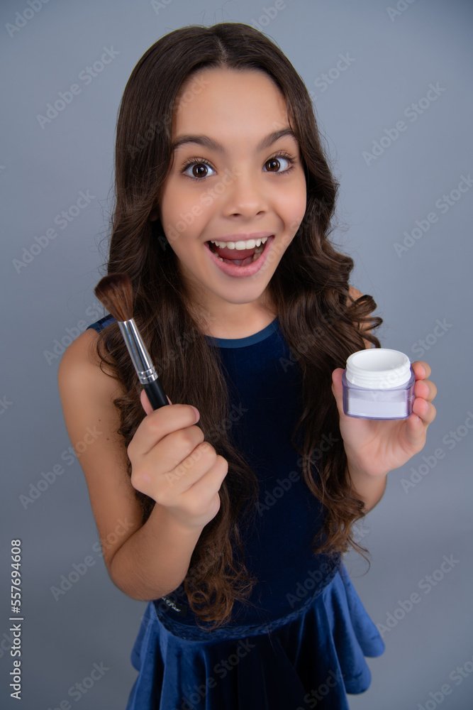 Beauty, make up and kids cosmetics. Teenage girl 12, 13, 14 years old with brush applying blush to face isolated on gray background. Excited face, cheerful emotions of teenager girl. Beauty, make up and kids cosmetics. Teenage girl 12, 13, 14 years old with brush applying blush to face isolated on gray background. Excited face, cheerful emotions of teenager girl.