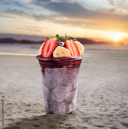 Photos A cup of acai topped with strawberry and banana on a beach at sunset