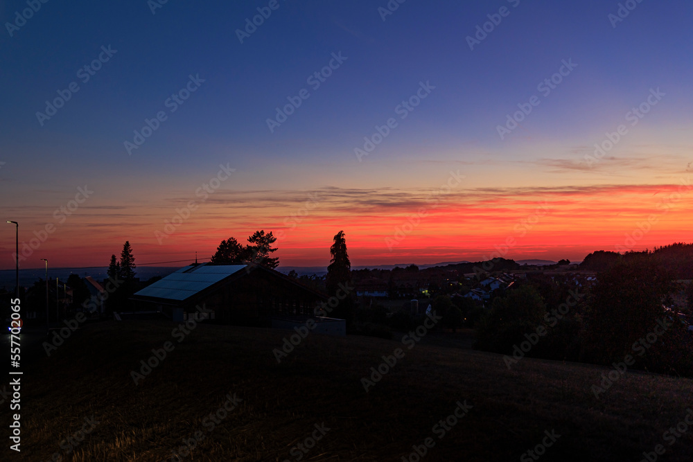colorful sunset in Rems-Murrkreis district in Germany with view of roof with solar panels and silhouette of tree