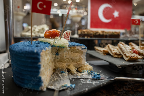 Close-up of half eaten layered cake with fruit slices and blue whipped cream on table in buffet with Turkish flag at restaurant