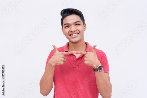 A young man makes the two fingers pointing gesture, trying to look shy. Uwu hand pose while smiling. Isolated on a white backdrop. photo