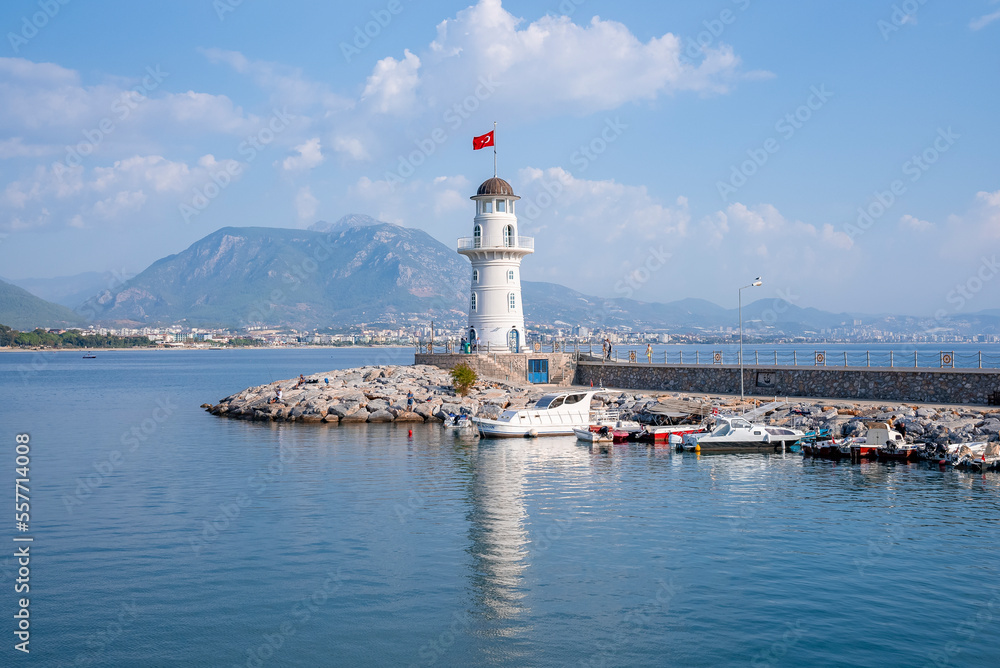 Side, Turkey. October 10, 2022. Alanya lighthouse with Turkish flag at port amidst beautiful seascape with mountain and cloudy sky in the background during sunny day