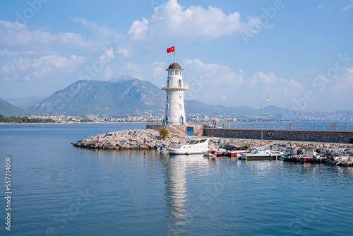 Side, Turkey. October 10, 2022. Alanya lighthouse with Turkish flag at port amidst beautiful seascape with mountain and cloudy sky in the background during sunny day