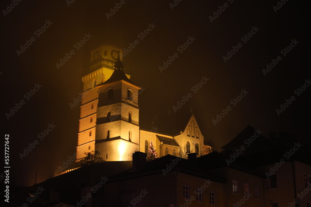 church of kremnica in dark night and fog with illumination and fountain with light in cold winter in slovakia