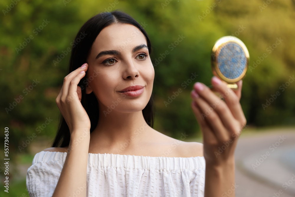 Beautiful young woman looking at herself in cosmetic pocket mirror outdoors Beautiful young woman looking at herself in cosmetic pocket mirror outdoors
